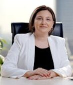 Professional woman in office, smiling and sitting at desk with laptop, showcasing success.