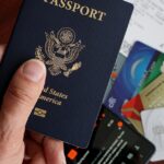 A close-up of a US passport with credit cards, tickets, and a mobile phone on a table.