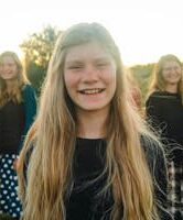 Outdoor group portrait of smiling teenage girl with friends in a field during sunset.
