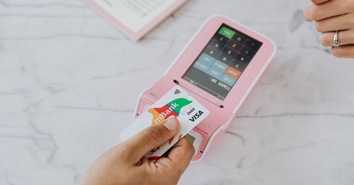 Hand using a contactless card on a pink POS terminal for a wireless transaction.