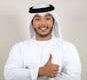 Portrait of a smiling man in traditional Emirati clothing giving a thumbs up against a white background.