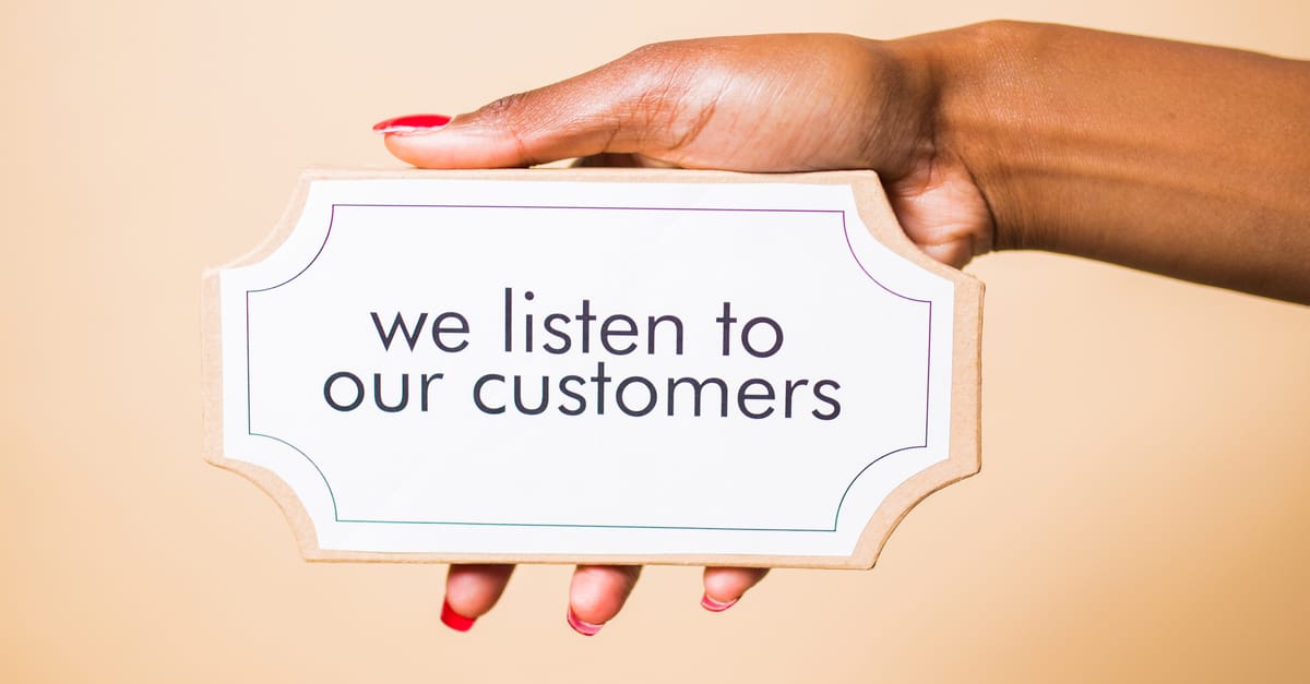 features A hand holding a sign saying 'we listen to our customers' on a neutral background.